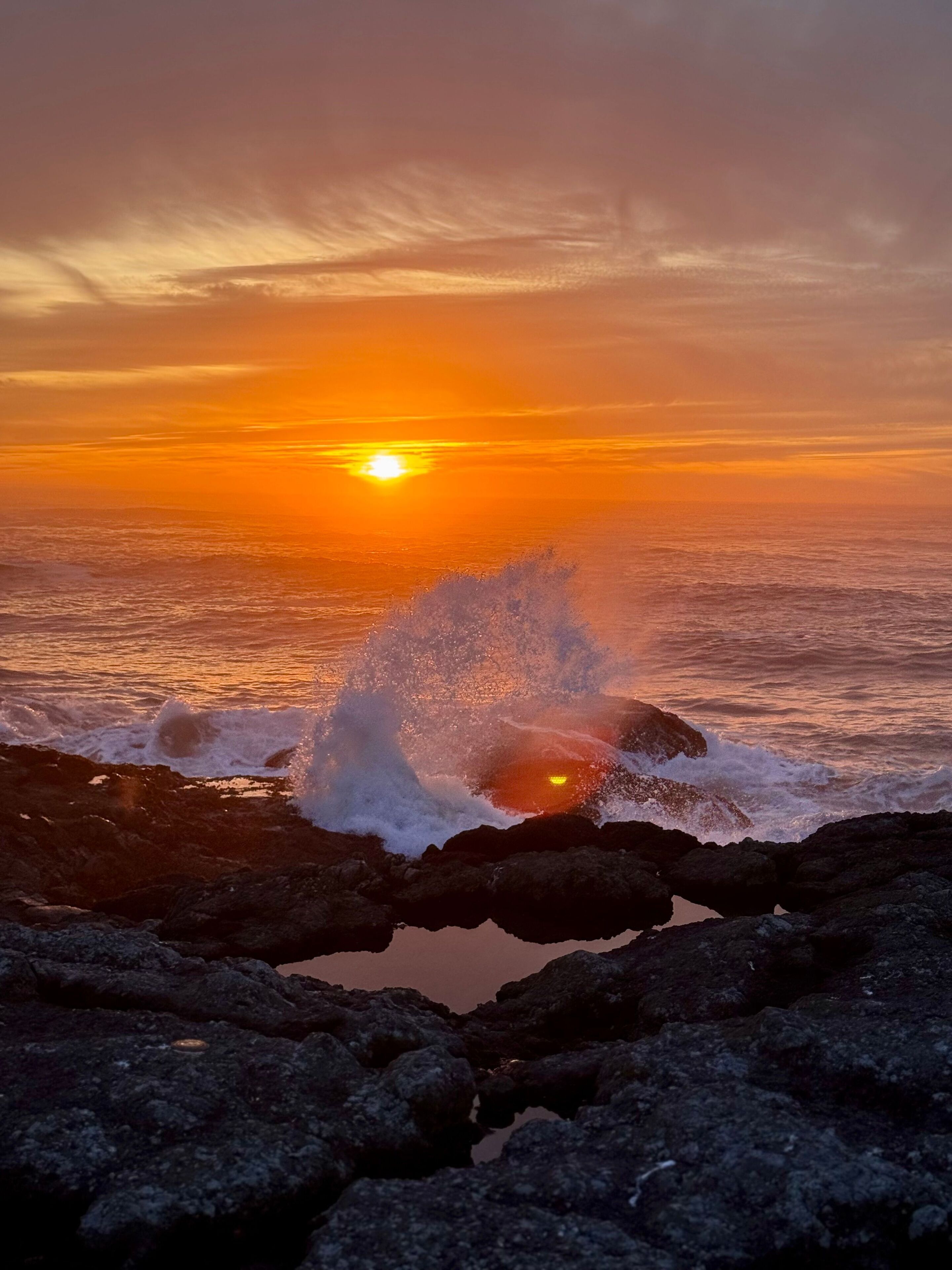 A sunset over a rocky coastline with waves crashing against the rocks.