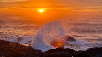 A sunset over a rocky coastline with waves crashing against the rocks.