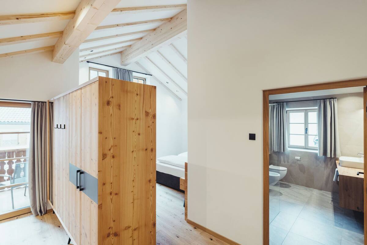Une chambre moderne avec des poutres en bois, un lit, une salle de bain et un balcon.