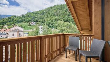 A wooden deck with two wicker chairs, overlooking a green hillside with houses.
