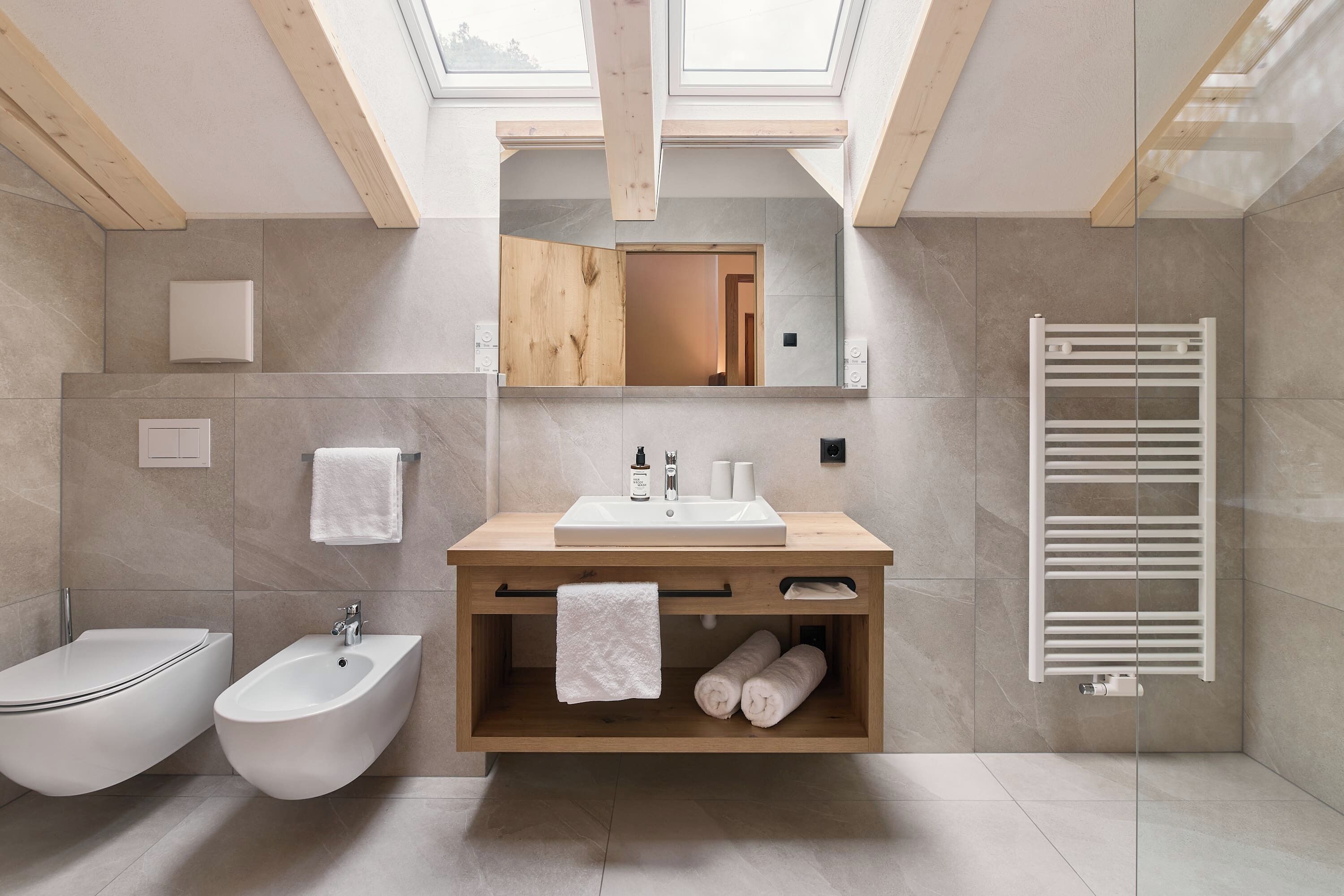 Un baño moderno con tragaluz, tocador de madera, bidé, tendedero para toallas y calentador de toallas.