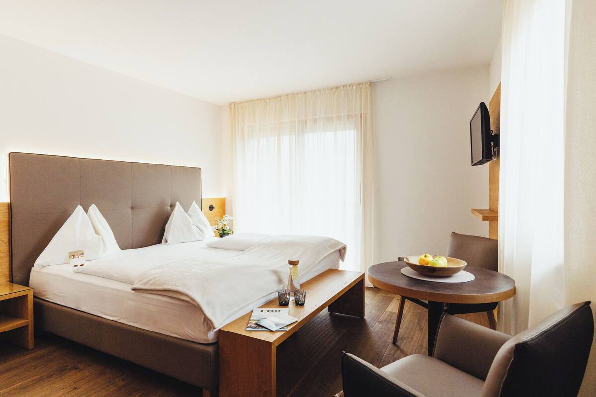 Une chambre d’hôtel avec un lit, une table de chevet, une chaise et une petite table sur laquelle se trouve un saladier rempli de fruits.