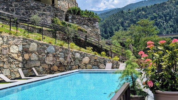 A swimming pool with stone walls and a stone building in the background. - Hotel Schmuckhof (Chiusa)