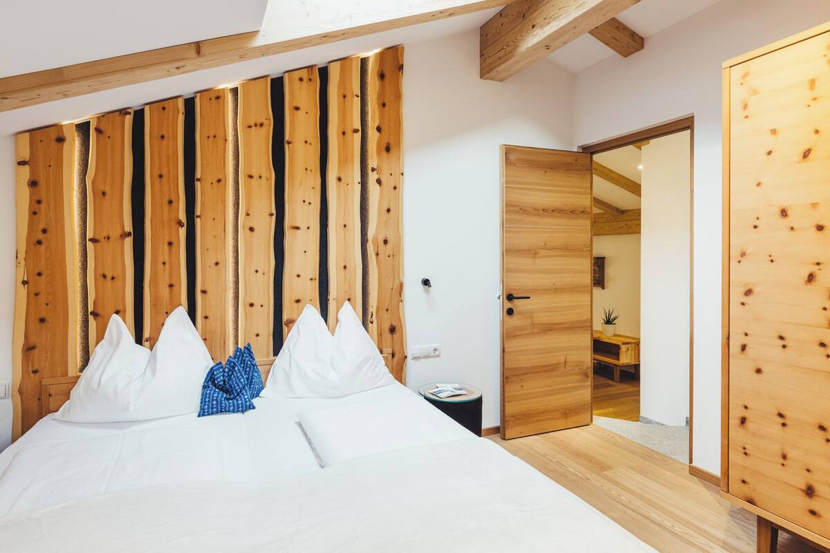 Une chambre avec une tête de lit en lattes de bois, un lit avec une literie blanche, une petite table de chevet avec un livre et une armoire en bois.