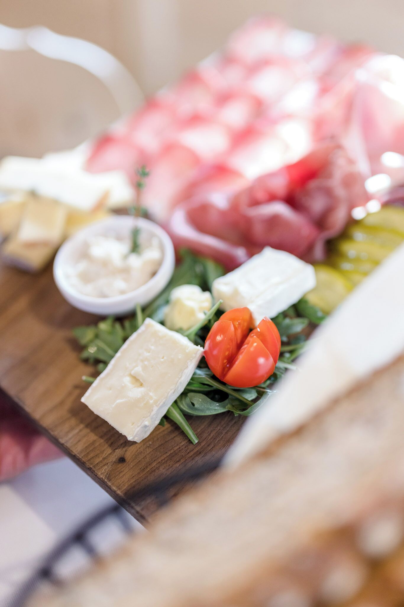 A wooden board with various cheeses, tomatoes, and a small bowl of dip.