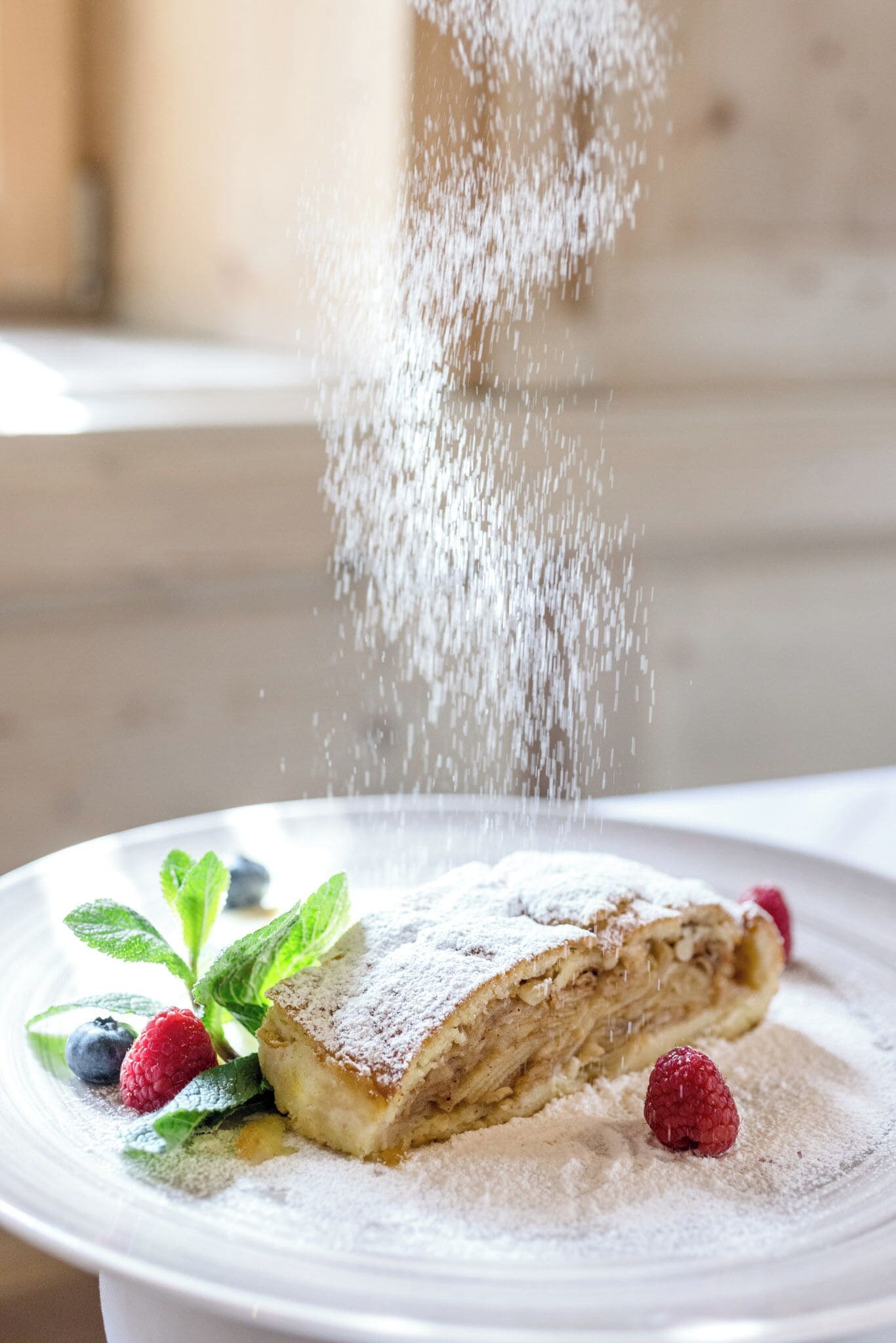 A dessert with powdered sugar, raspberries, and mint leaves on a white plate.