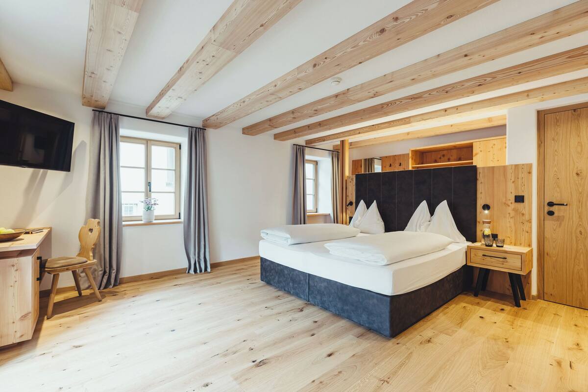 Une chambre à coucher avec un lit, des poutres en bois, un bureau et un téléviseur.