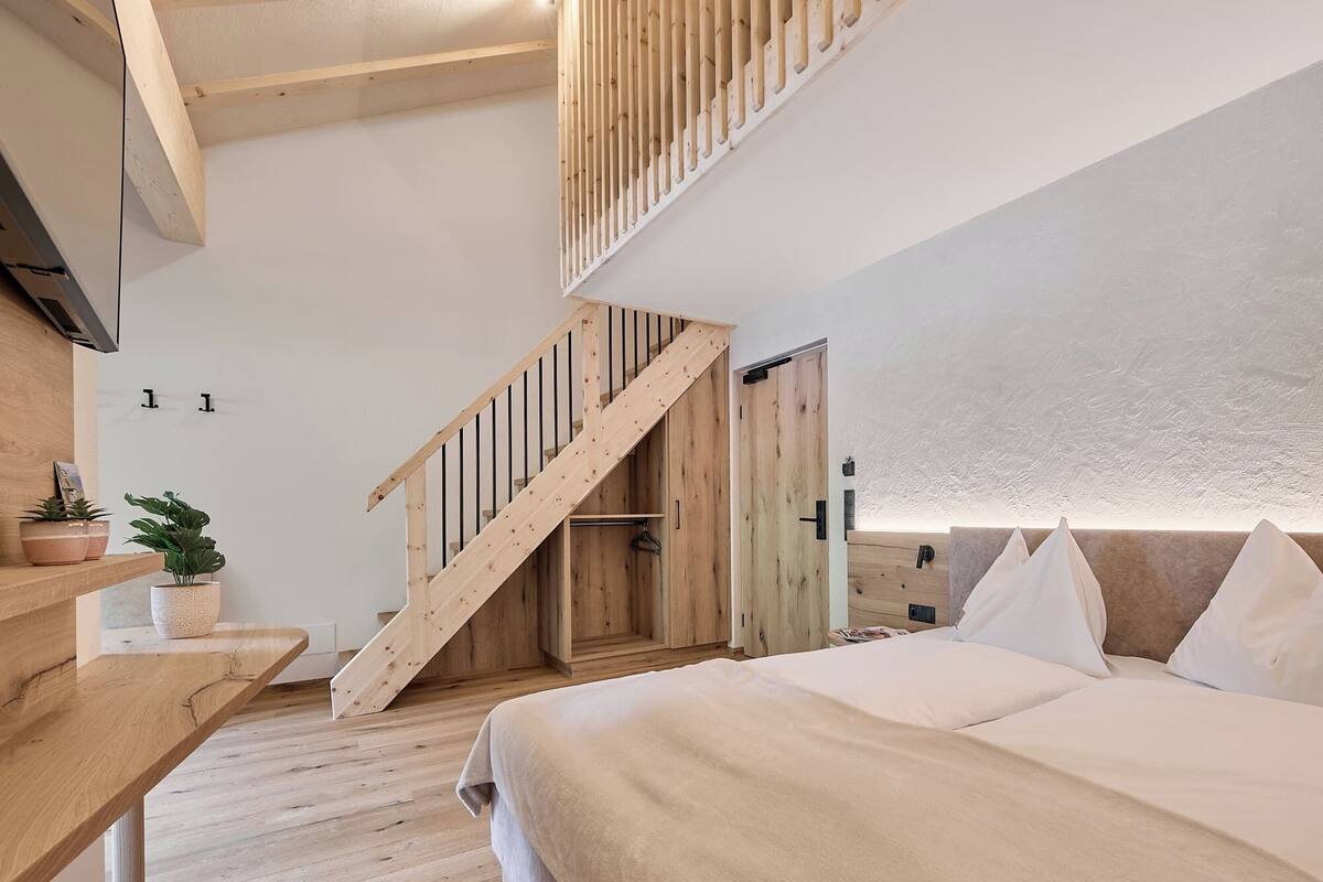 Une chambre avec un escalier en bois, un lit avec une literie blanche et une petite plante posée sur une table de chevet.