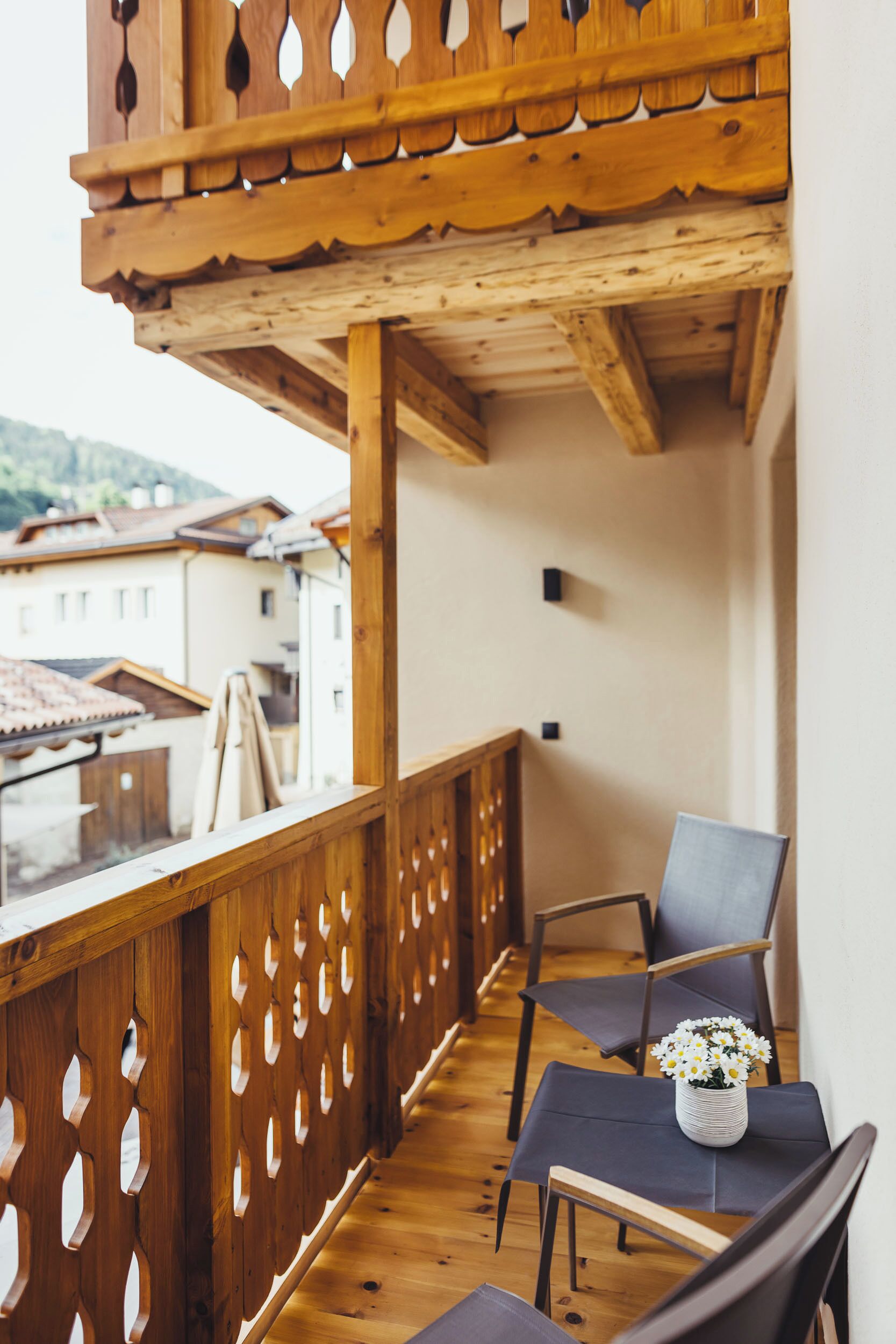 Een balkon met houten hekwerk, een tafel met stoelen en een vaas met bloemen.