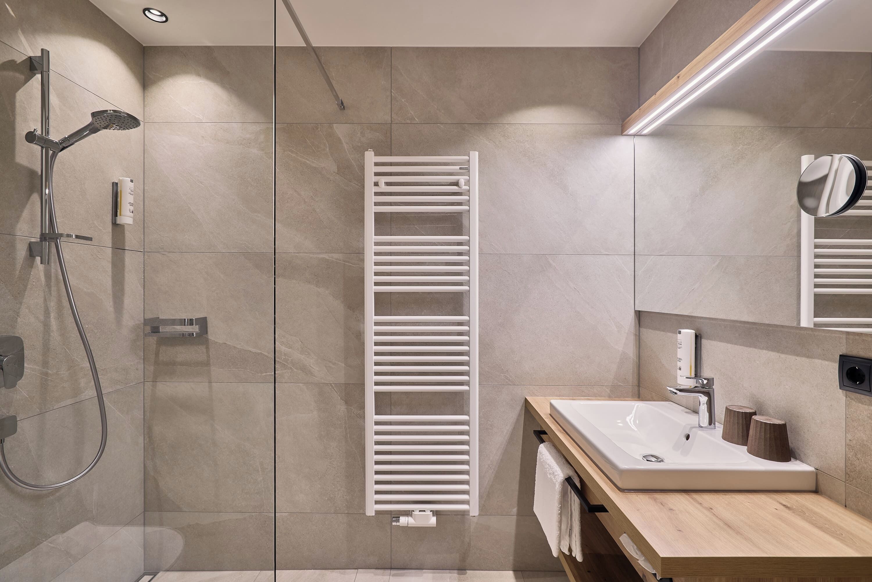 Een moderne badkamer met een douchecabine van glas, een witte handdoekhouder, een houten wastafelmeubel met een wastafel en een spiegel.