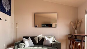 Un salon avec un canapé gris, une petite table et un miroir au mur.