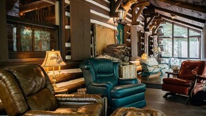 A cozy room with leather sofas, a wooden coffee table, and a rustic wooden ceiling. - Secluded 10-Acre Riverfront Lodge. Pet-Friendly! Hot Tub! (Traverse City)