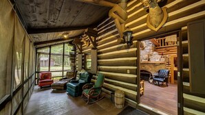 A log cabin interior with a cozy seating area, wooden walls, and a stone fireplace. - Secluded 10-Acre Riverfront Lodge. Pet-Friendly! Hot Tub! (Traverse City)