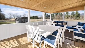Eine überdachte Terrasse mit Holzboden, weißer Möbel und Blick auf eine ländliche Landschaft.
