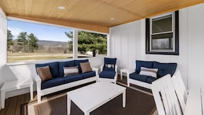 Ein überdachter Außenbereich mit einer blauen Couch, weißen Stühlen und einem weißen Tisch.