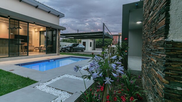 Ein modernes Haus mit Schwimmbad, einem geparkten Auto und einer Steinmauer.