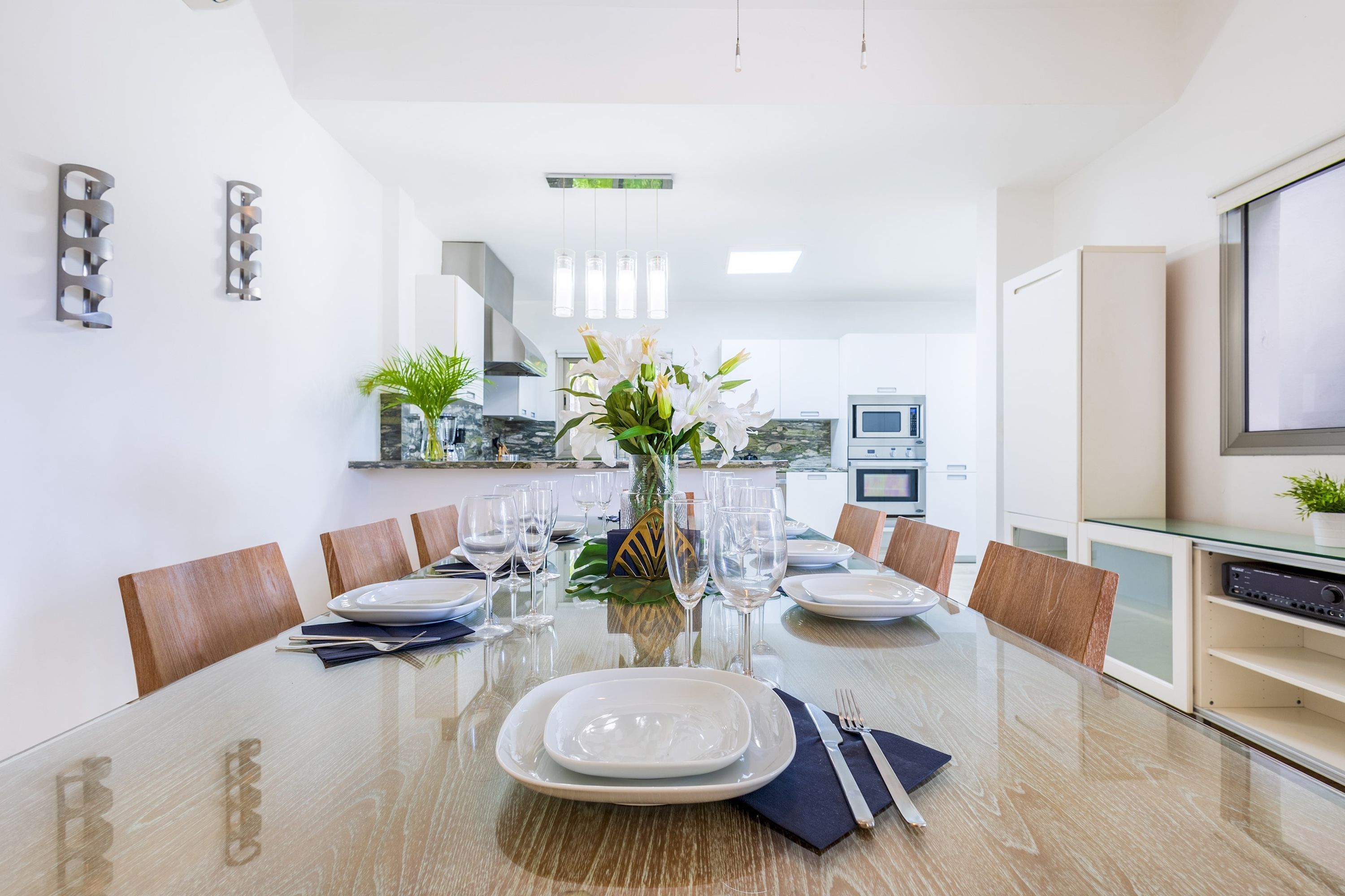 A modern dining room with a glass table, white plates, and a vase of flowers.