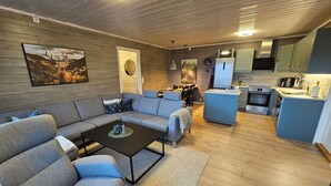 A modern living space with a grey sofa, a coffee table, and a kitchen area with a fridge, oven, and sink. - Cozy 7-bed Bavallen apartment near Voss Resort – family ski base (Vestland)