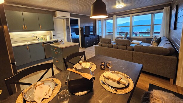 A modern kitchen with dark cabinets and a dining area set for a meal. - Cozy 7-bed Bavallen apartment near Voss Resort – family ski base (Vestland)