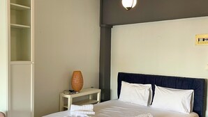 En pænt redt seng med hvide sengetøj, en mørk sengegavl og et natbord med en lampe.