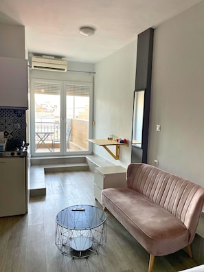 Ein modernes Wohnzimmer mit einer Couch, einem Glastisch und einer Küchenzeile mit Herd.