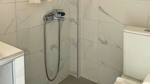 Et badeværelse med bruser, toilet og et vindue.