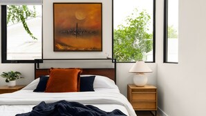 A bedroom with a bed, a nightstand, a lamp, a painting, and a window with a view of trees. - Eastside Lux Group  W Pool near Downtown (Austin)