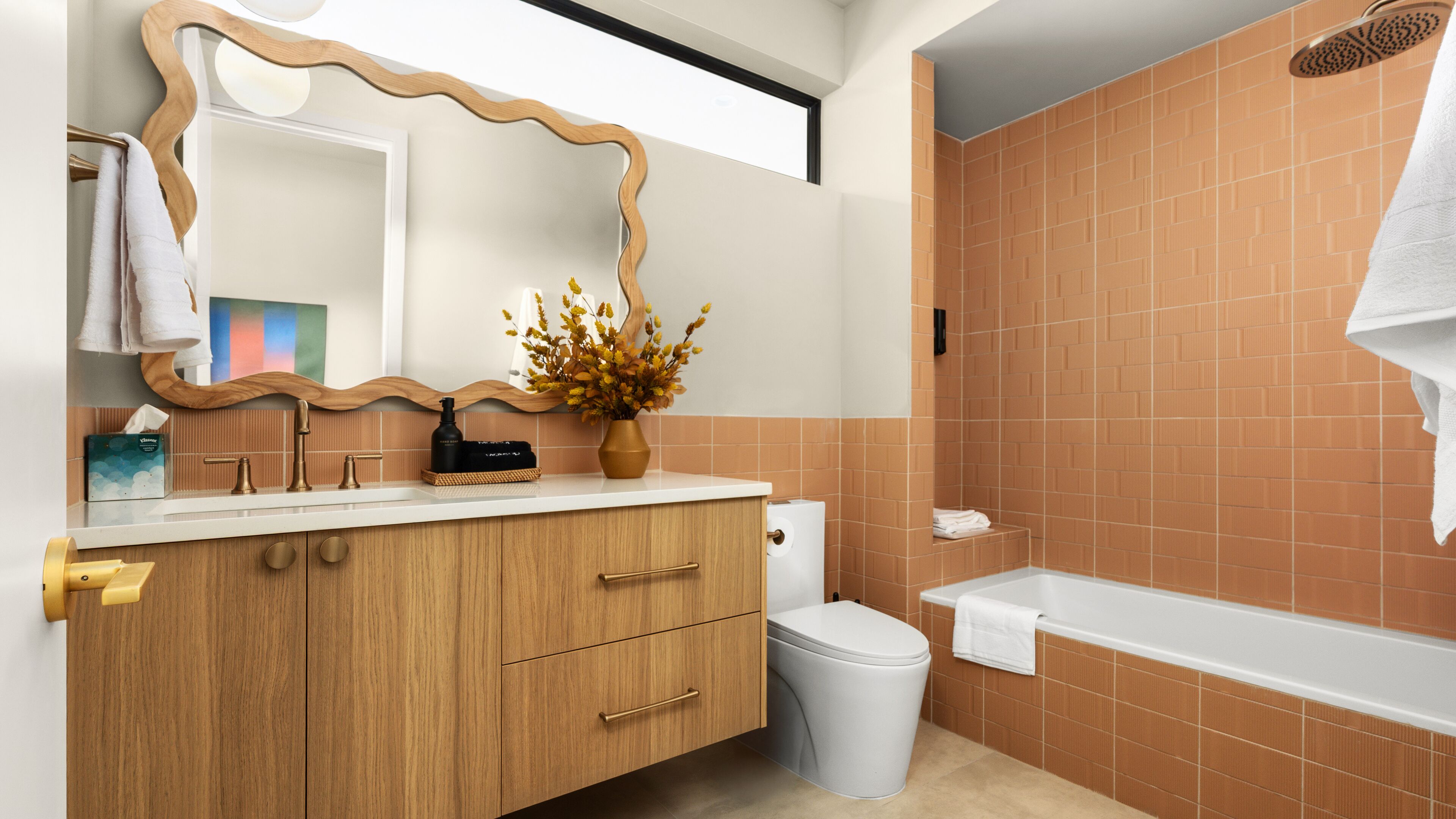 Un baño con un tocador de madera, un inodoro blanco, una bañera blanca y un espejo grande con marco de madera.