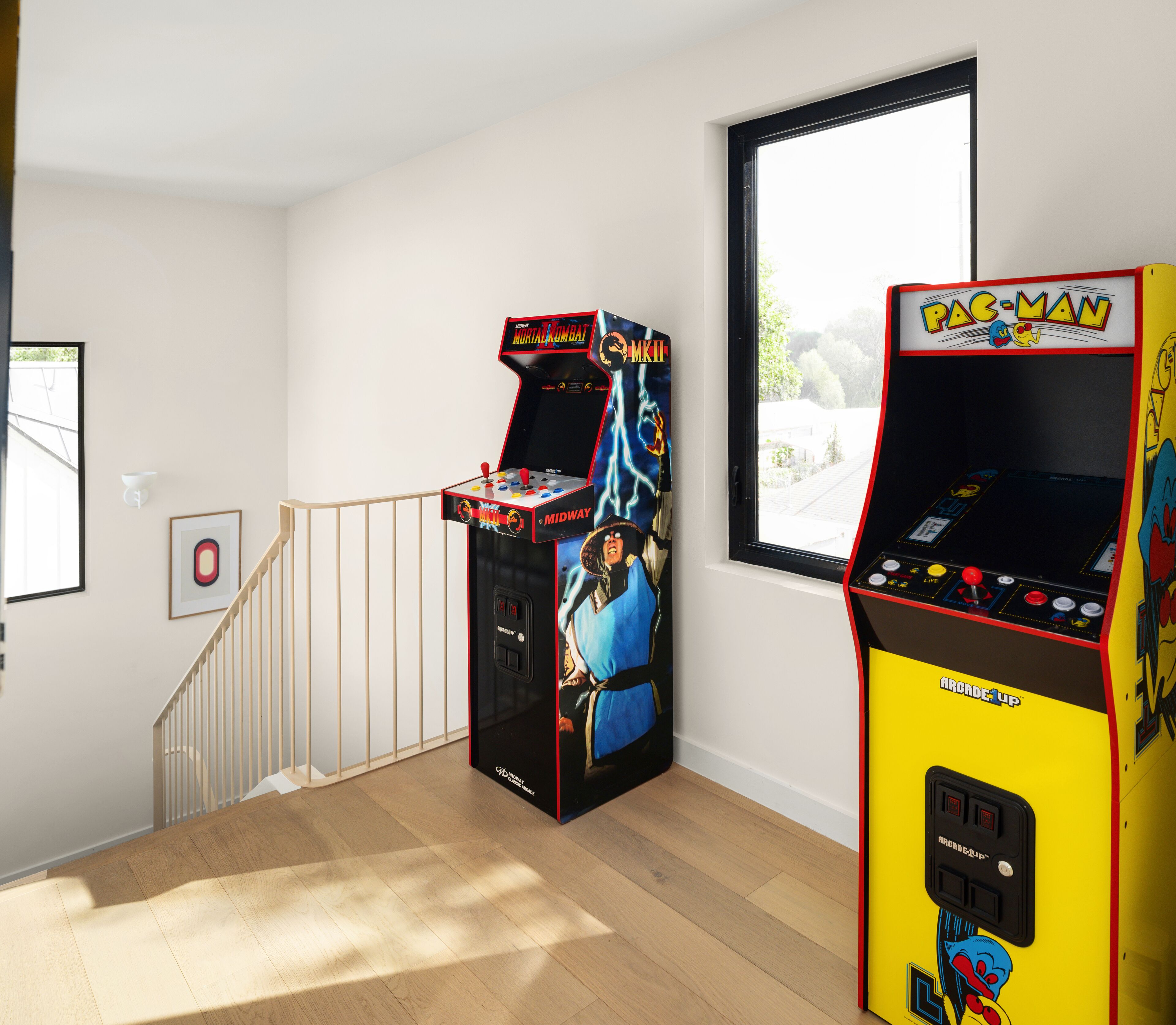 Una habitación con dos máquinas de videojuegos, una escalera y un ventanal.