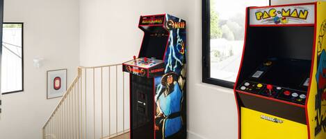 Una habitación con dos máquinas de videojuegos, una escalera y un ventanal.