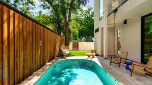 A swimming pool with a wooden fence, outdoor seating, and a building with balconies. - Eastside Lux Group  W Pool near Downtown (Austin)