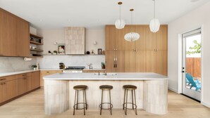 A modern kitchen with wooden cabinets, a marble countertop, and a central island with stools. - Eastside Lux Group  W Pool near Downtown (Austin)