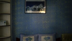 Een slaapkamer met een lijst met een foto van de Mount Everest, een kalender en twee sierkussens met bloemmotieven.
