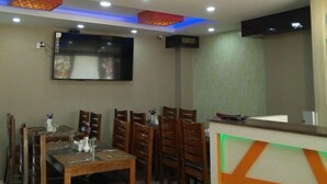 A dining area with a table and chairs, a flat-screen TV mounted on the wall, and decorative ceiling panels. - Hotel Marinha Pvt. Ltd (Kathmandu)