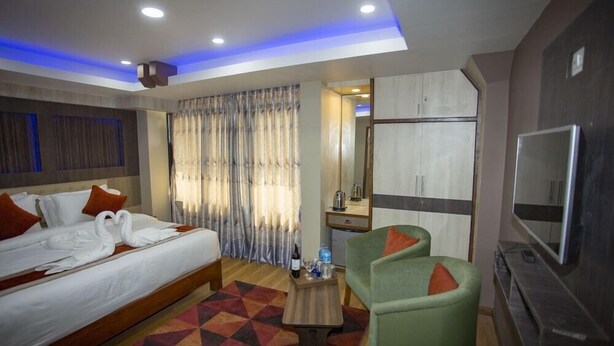 A hotel room with a bed, a green armchair, a TV, and a minibar. - Hotel Marinha Pvt. Ltd (Kathmandu)