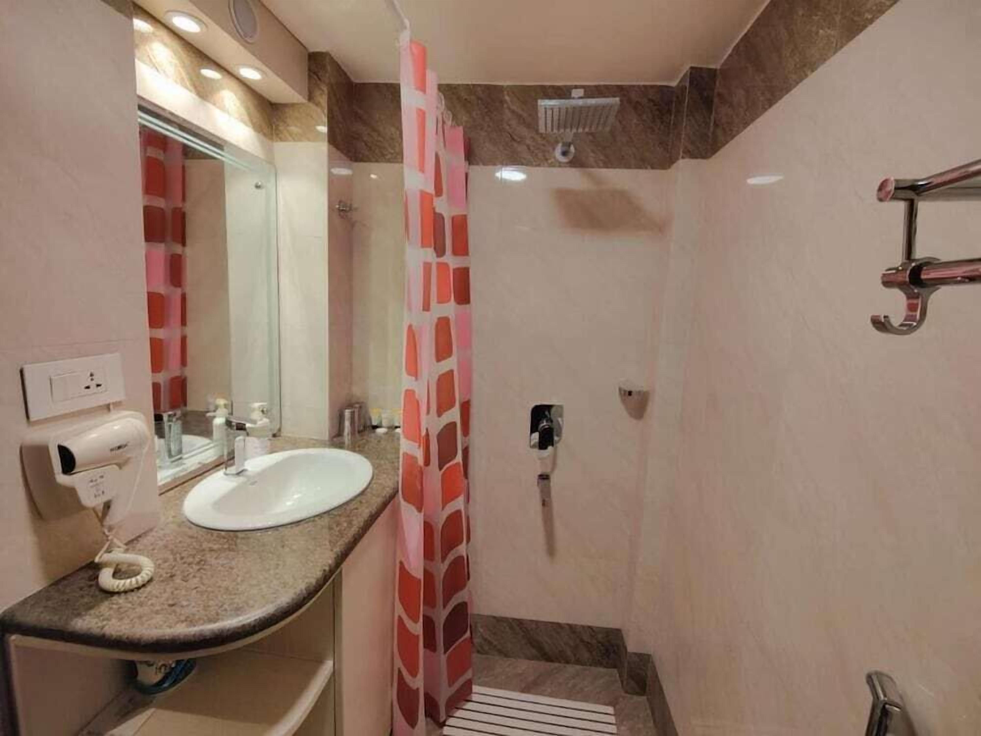 A bathroom with a sink, mirror, shower, and towel rack.