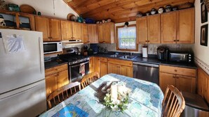 Une cuisine avec des meubles de rangement en bois, un réfrigérateur, une cuisinière et une table à manger recouverte d’une nappe à motifs floraux.