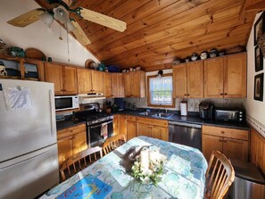 A kitchen with wooden cabinets, a refrigerator, a stove, and a dining table with a floral tablecloth. - Welcoming 3-bedroom house with AC in Dennis Port, close to beaches (Dennis)