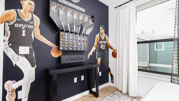 A basketball-themed room with a large mural of a player, a Connect 3 game board, and a basketball hoop. - *D-town/Photobooth/Glam Rm* (San Antonio)