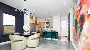 A modern kitchen with a dining area, featuring a central island, bar stools, and a colorful abstract painting on the wall. - *D-town/Photobooth/Glam Rm* (San Antonio)