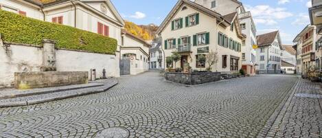 A cobblestone street with traditional European architecture, including a building with a balcony and a sign for a hotel.