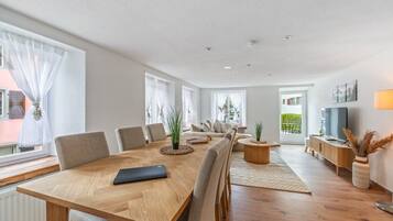Ein modernes Wohnzimmer mit Esstisch aus Holz, Sofas und einem Fernseher.