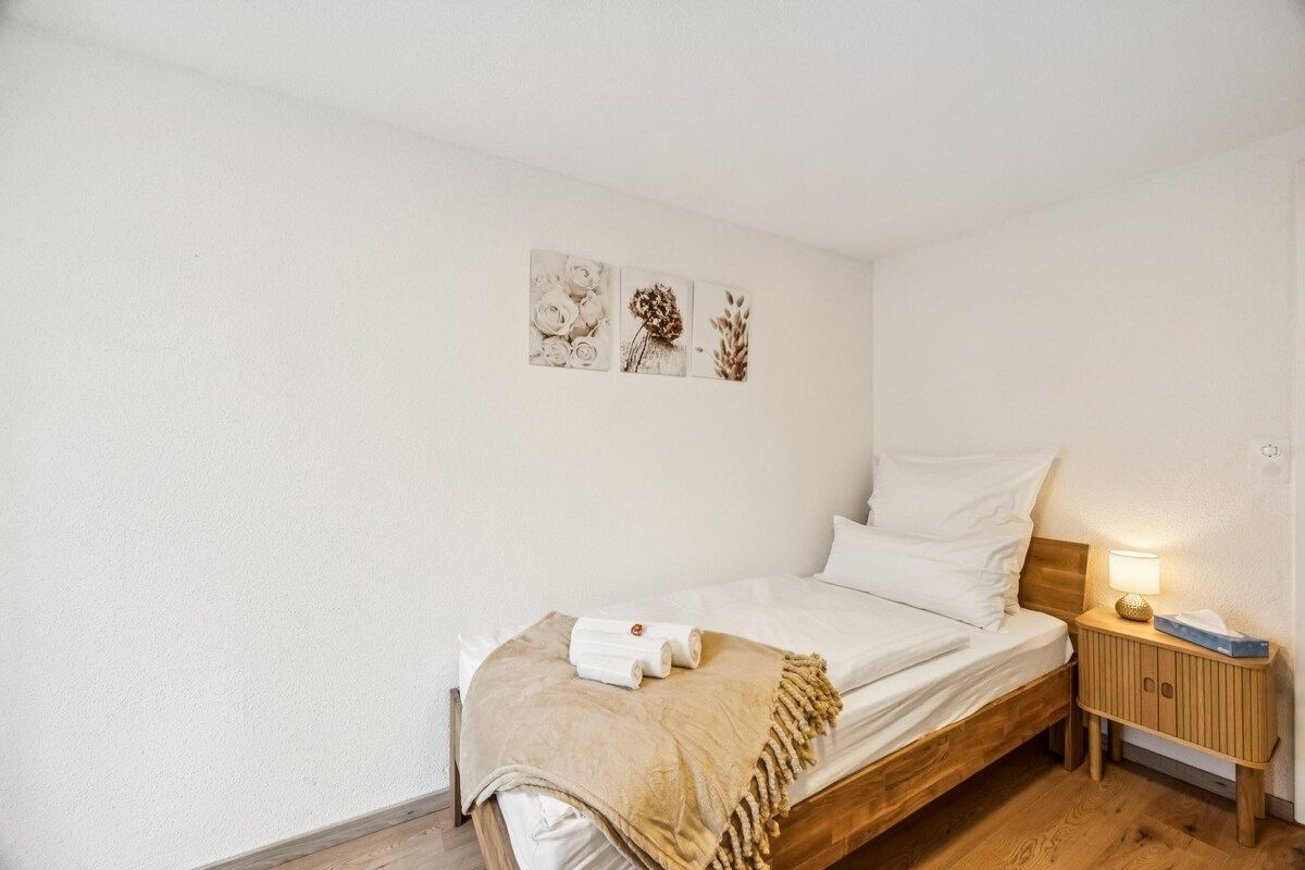 Ein Einzelbett mit Holz Kopfteil, ein Nachttisch mit Lampe und Wandbild über dem Bett.