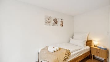 Ein Einzelbett mit Holz Kopfteil, ein Nachttisch mit Lampe und Wandbild über dem Bett.