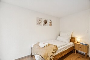 Una cama individual con cabecera de madera, una mesita de noche con lámpara y un cuadro en la pared sobre la cama.