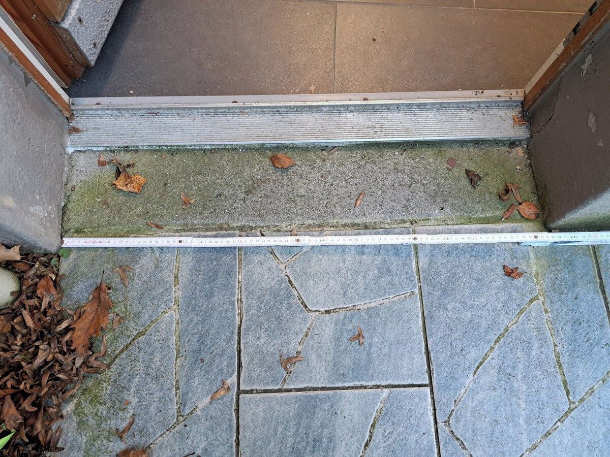 Una entrada con baldosas de piedra, un umbral metálico y un metro.