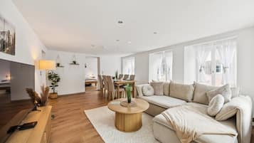 Ein modernes Wohnzimmer mit einer Couch, einem Couchtisch und einem Essbereich im Hintergrund.