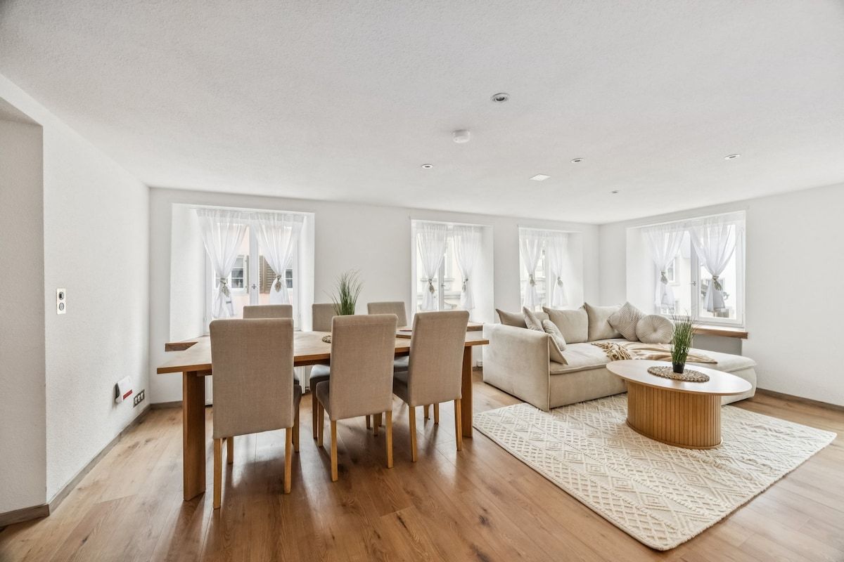 Ein modernes Wohnzimmer mit Essbereich, ausgestattet mit einem Holztisch, Stühlen, einer Couch und einem Couchtisch.