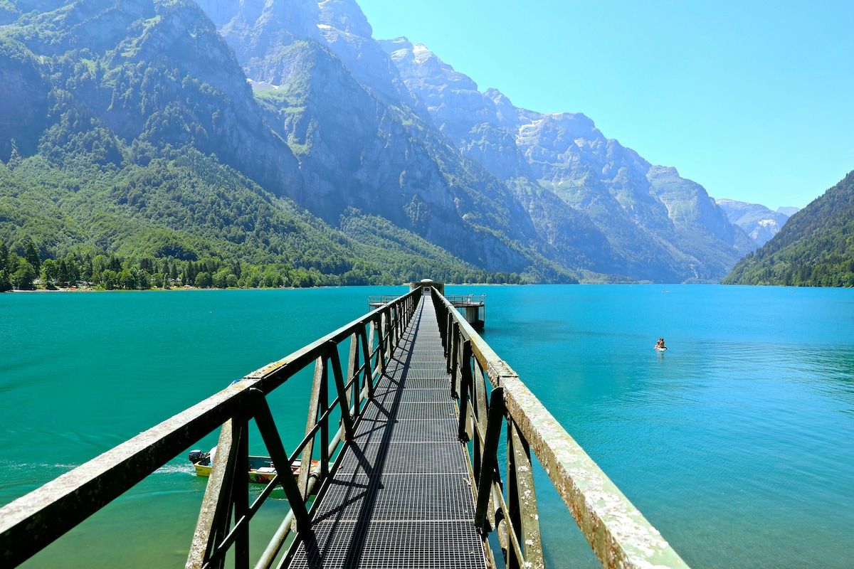 Un muelle de madera que se adentra en un lago turquesa con montañas al fondo.