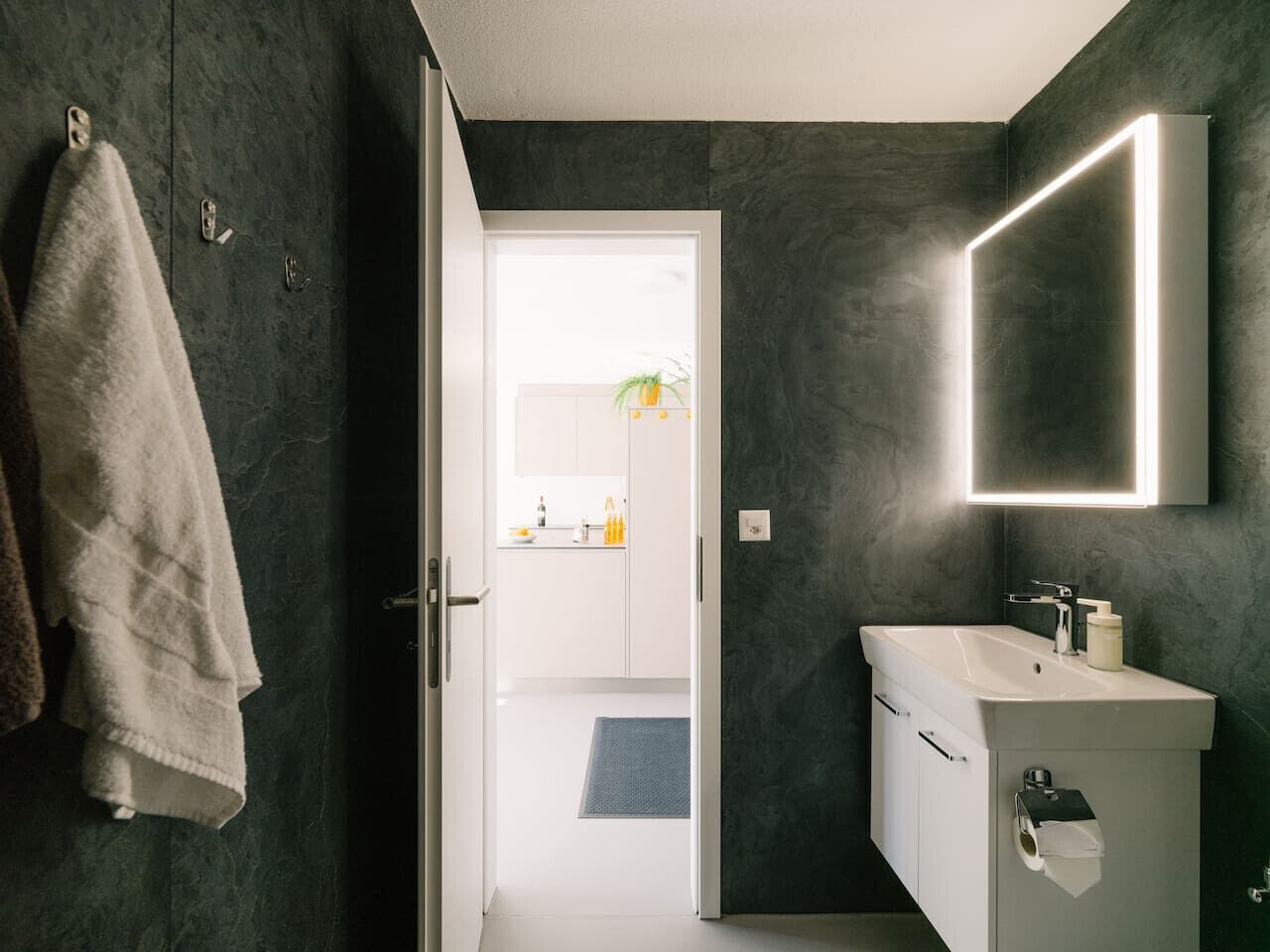 A modern bathroom with dark walls, a white sink, and a mirror.
